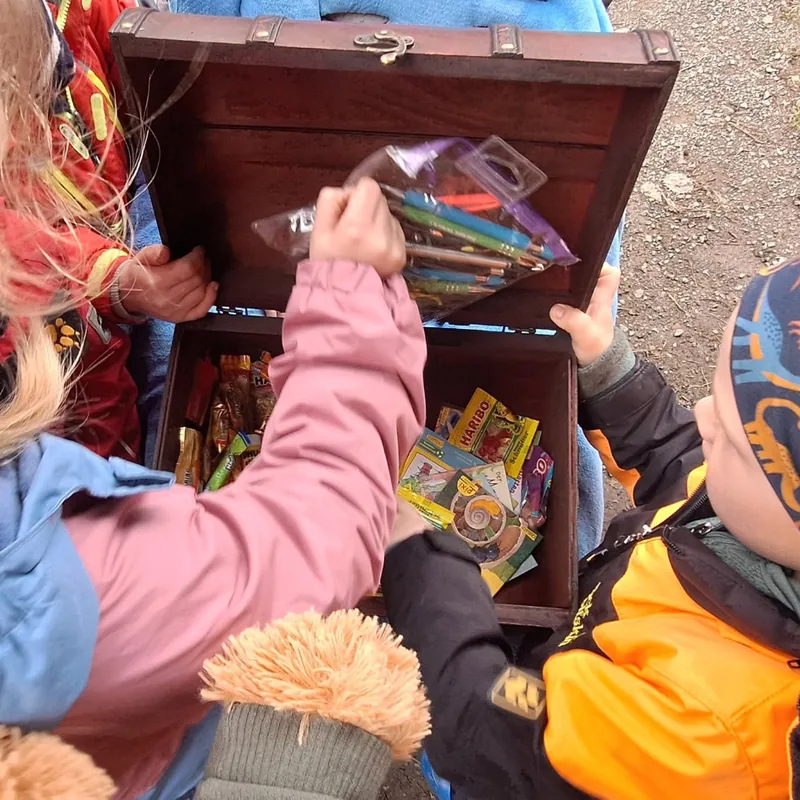 Kinder öffnen gemeinsam eine gefüllte Schatzkiste, ihre Gesichter sind nicht zu sehen