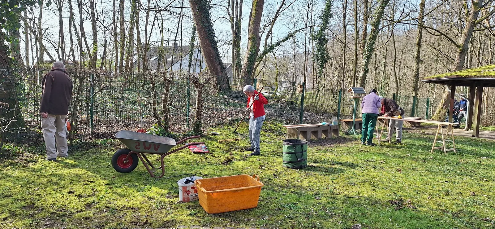 Mitglieder pflegen den Rasen und bearbeiten Holzbretter neben dem Grillpavillon.