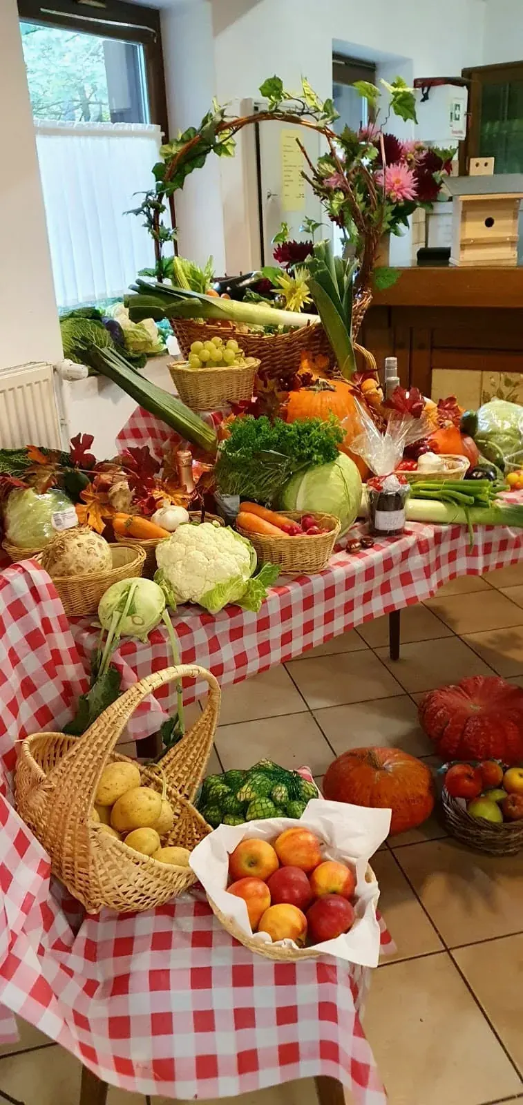 Körbe mit Äpfeln, Kartoffeln und Gemüse neben Kürbissen und Blumen.