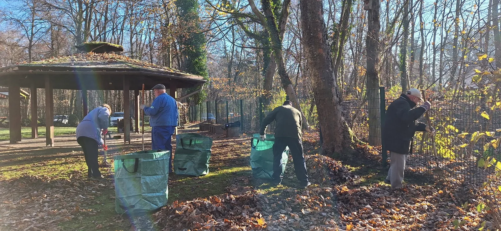 Mitglieder arbeiten mit Rechen und Gartensäcken auf dem Außengelände.