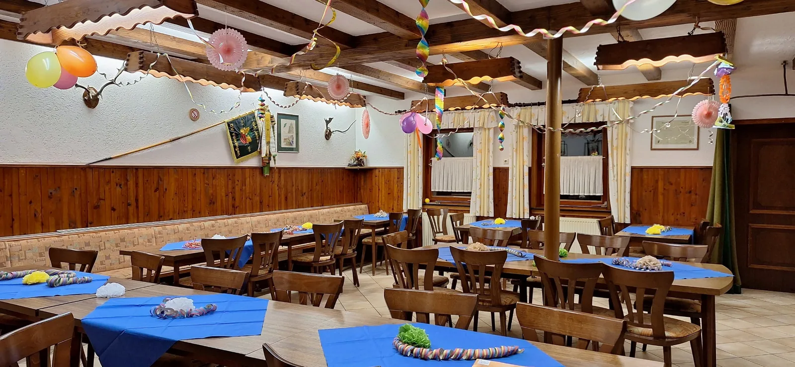 Saal des Kreuzberghauses mit Luftballons, Girlanden und blauen Tischdecken.