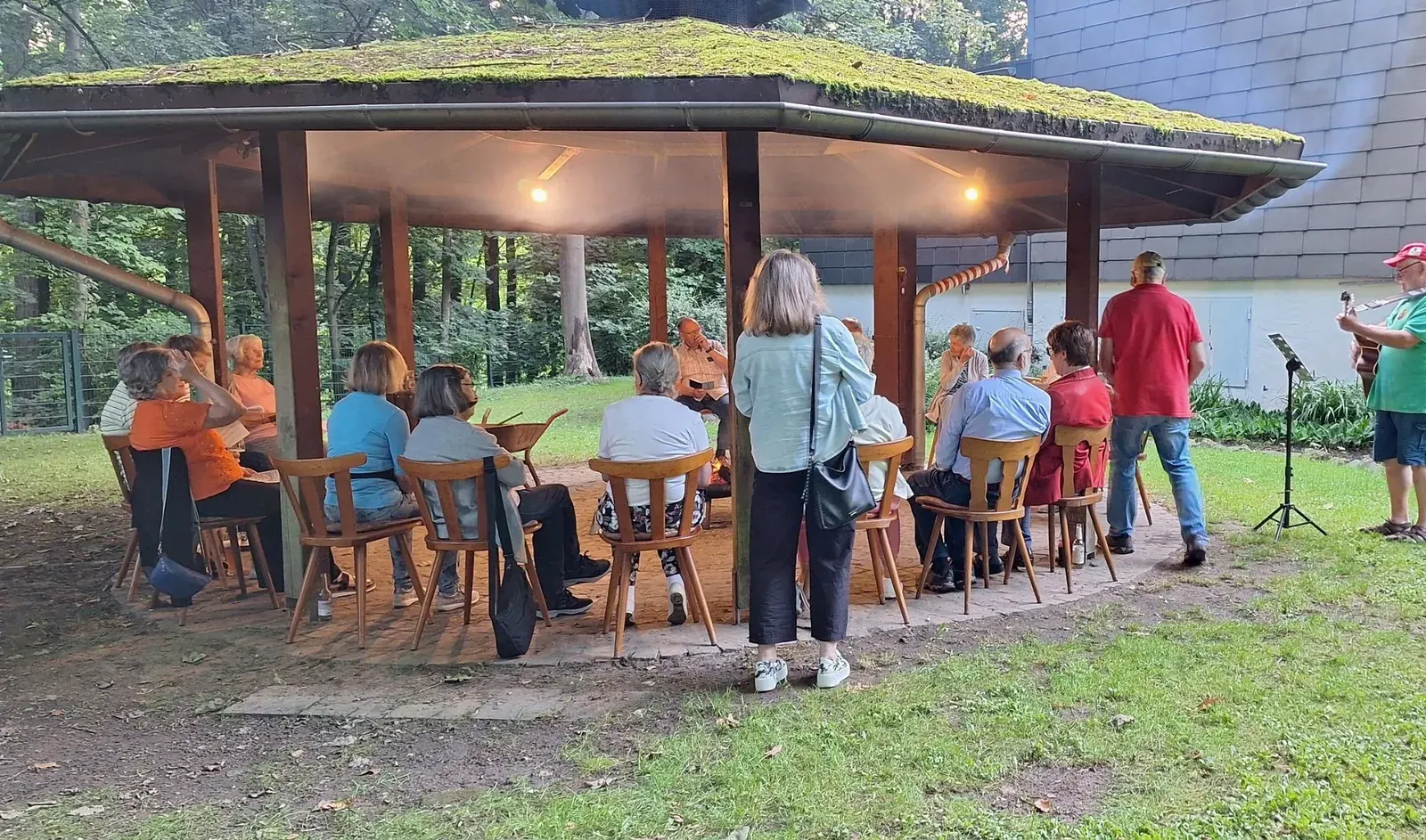 Eine gesellige Runde sitzt im Grillpavillon, rechts spielt ein Gitarrist.