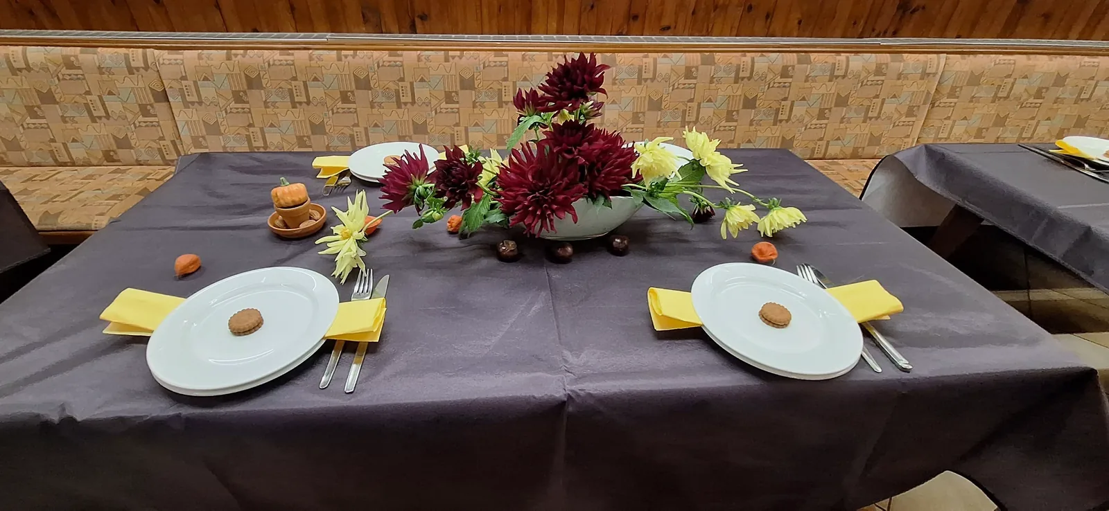 Gedeckter Tisch mit gelben Servietten, Dahlien und kleinen Kürbissen.