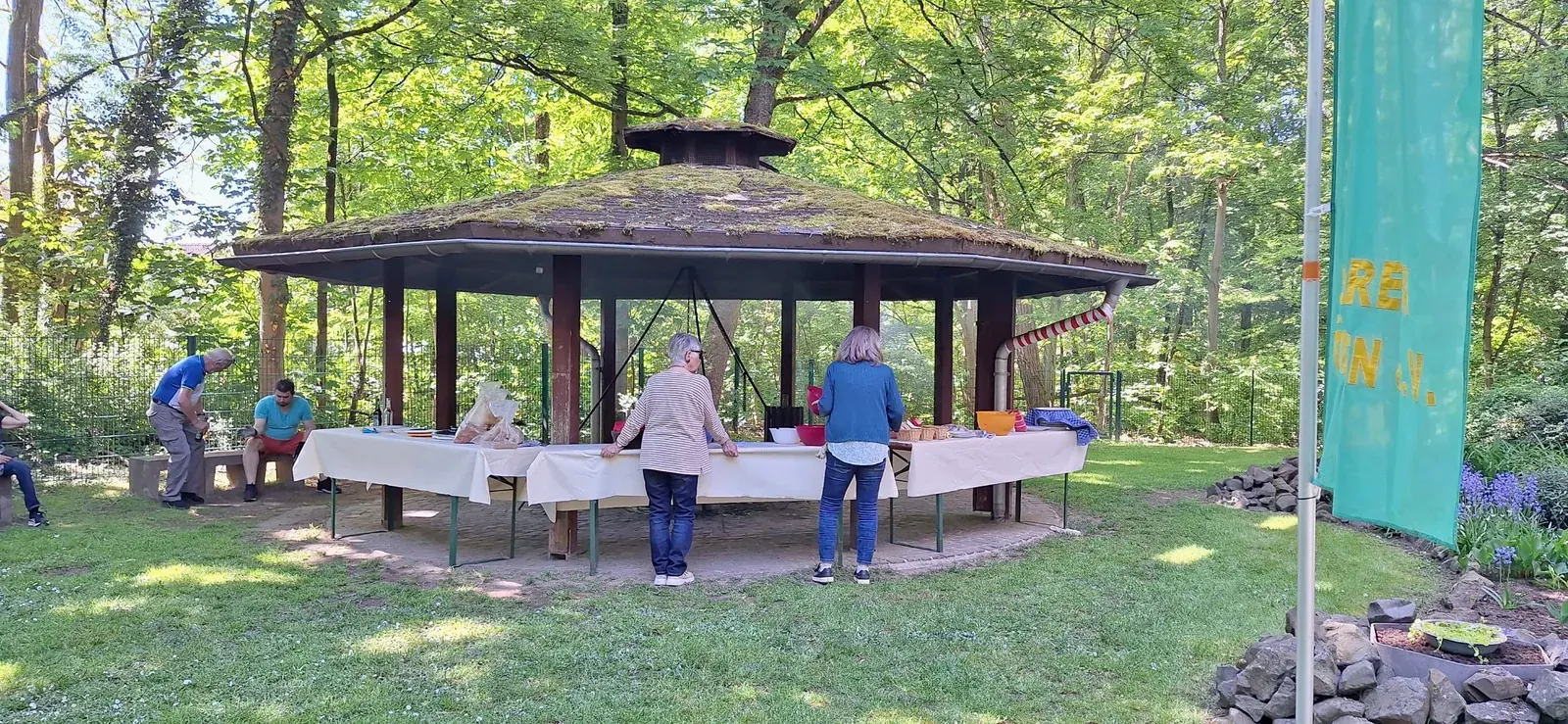 Mitglieder bereiten Tische mit Speisen am Grillpavillon vor.