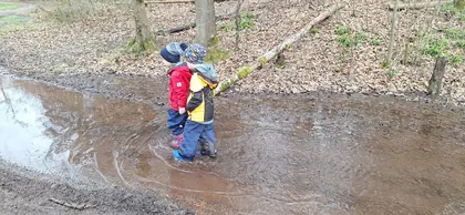 Zwei Kinder entdecken bei einer Familienwanderung eine große Pfütze im Wald
